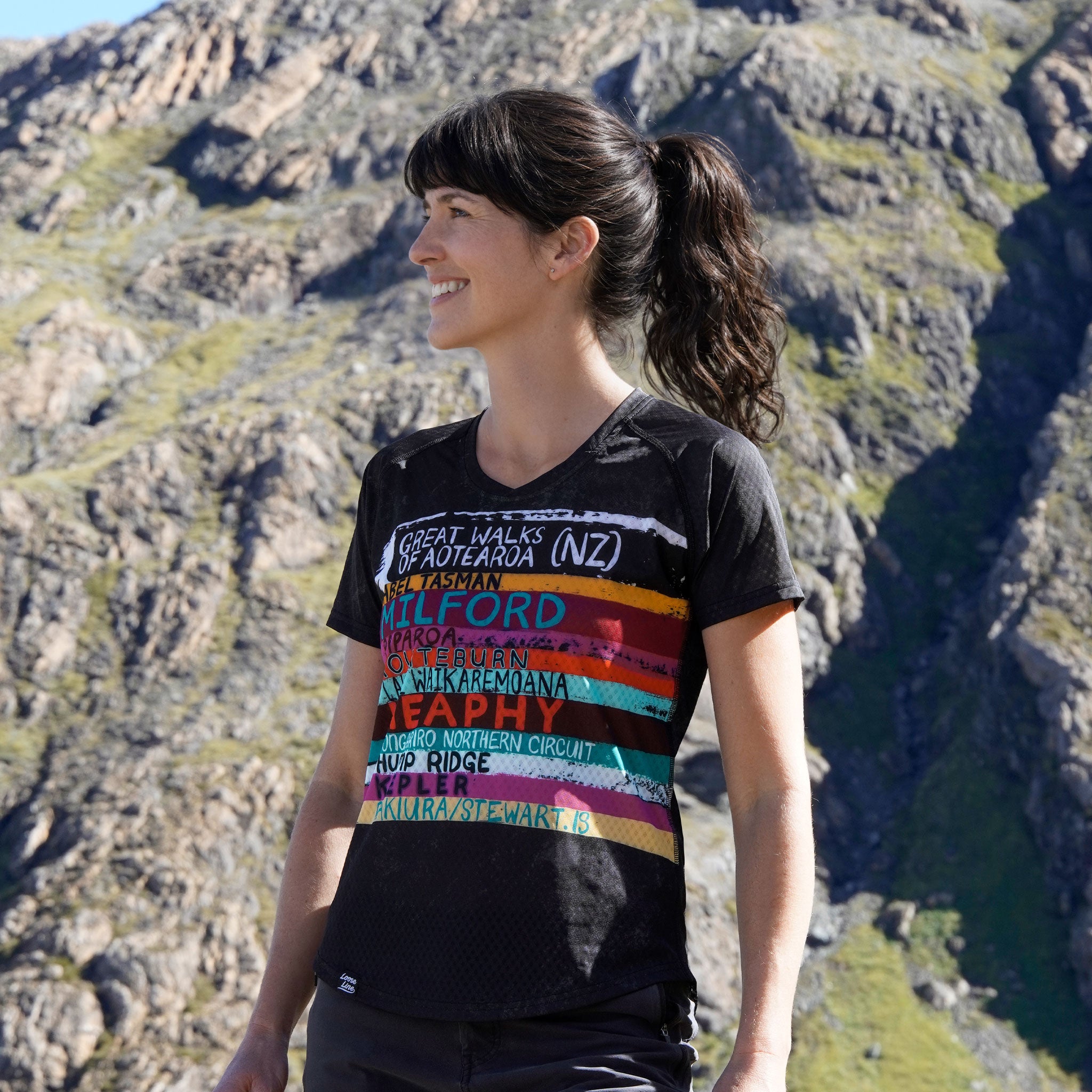 Woman wearing the great walks of aotearoa t-shirt standing on a mountain.