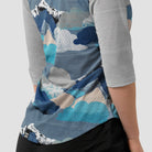 Woman wearing a shirt with a mountain and cloud pattern on a textured background made up of brushstokes.