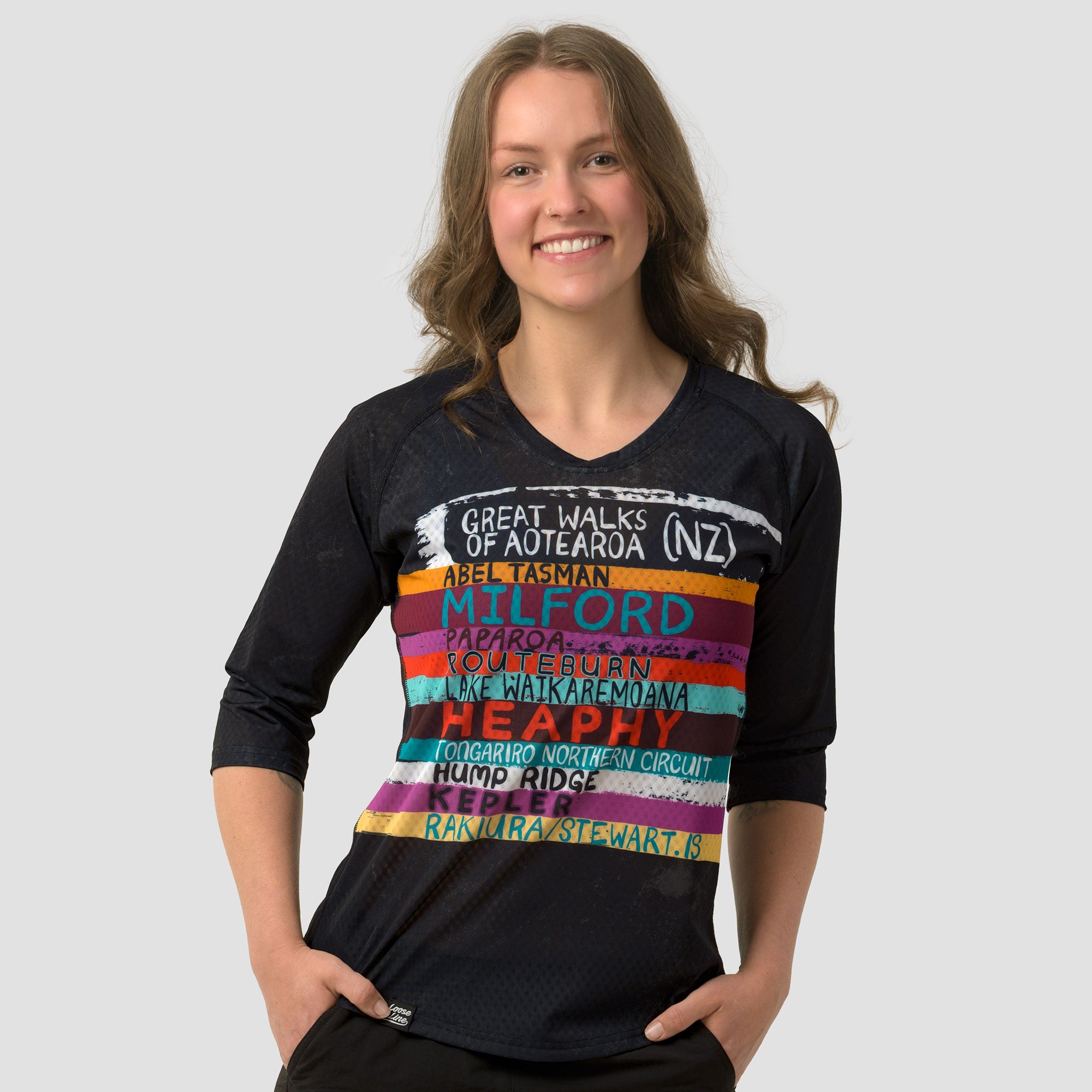 Woman wearing a black 3/4 sleeve activewear top featuring the great walks of New Zealand featuring colourful brushstrokes with each great walk listed.
